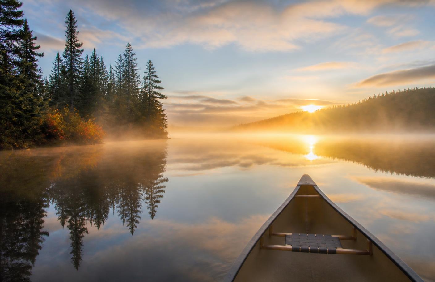 Canoe on a calm Canadian lake at sunrise with mist over the water